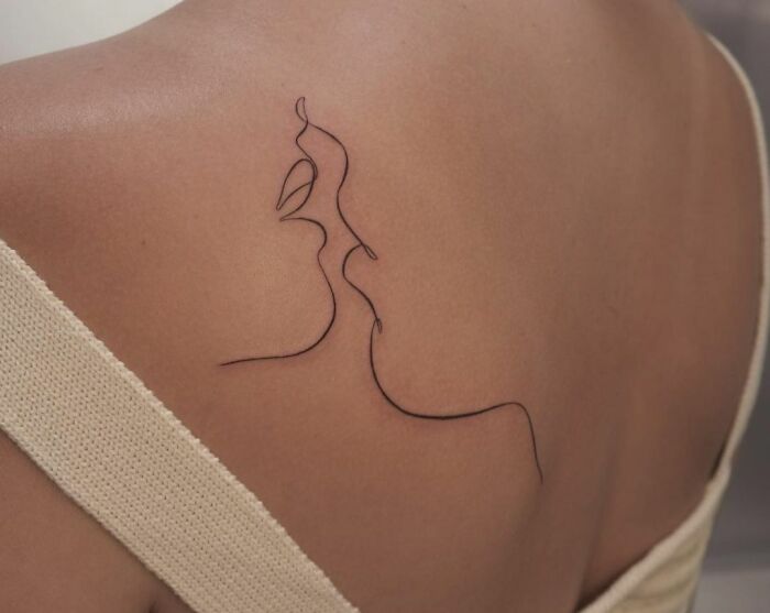Minimalist line tattoo of abstract faces on a person's shoulder.
