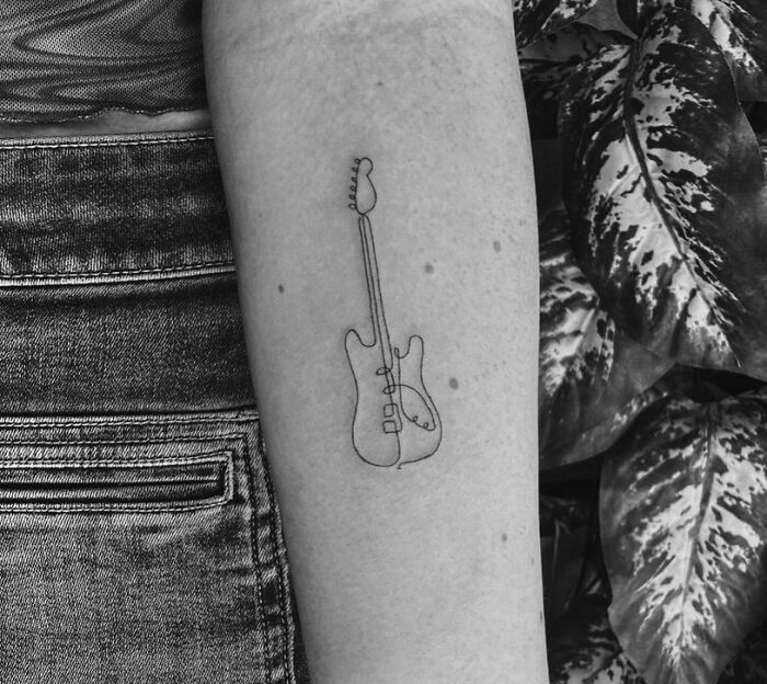 Minimalist line tattoo of a guitar on a forearm, showcasing unique tattoo ideas for minimalism enthusiasts.