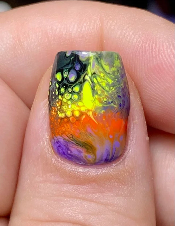 Colorful abstract nail art design with vibrant swirls of yellow, orange, and purple on a fingernail.