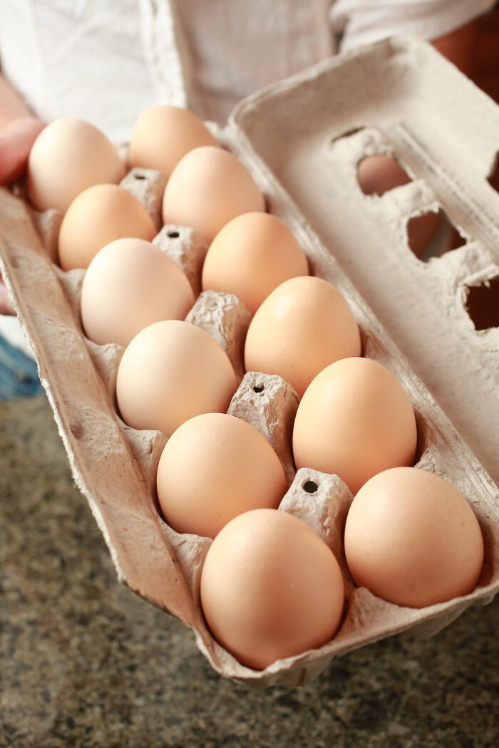Carton of fresh brown eggs held by a person, illustrating peasant food products many can no longer afford.