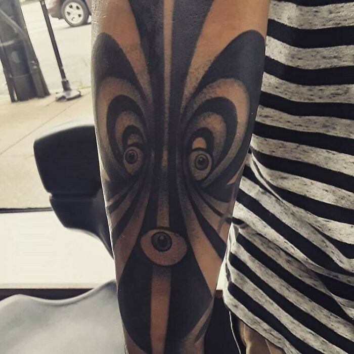 Optical illusion tattoo design on arm with abstract black and gray swirling patterns.