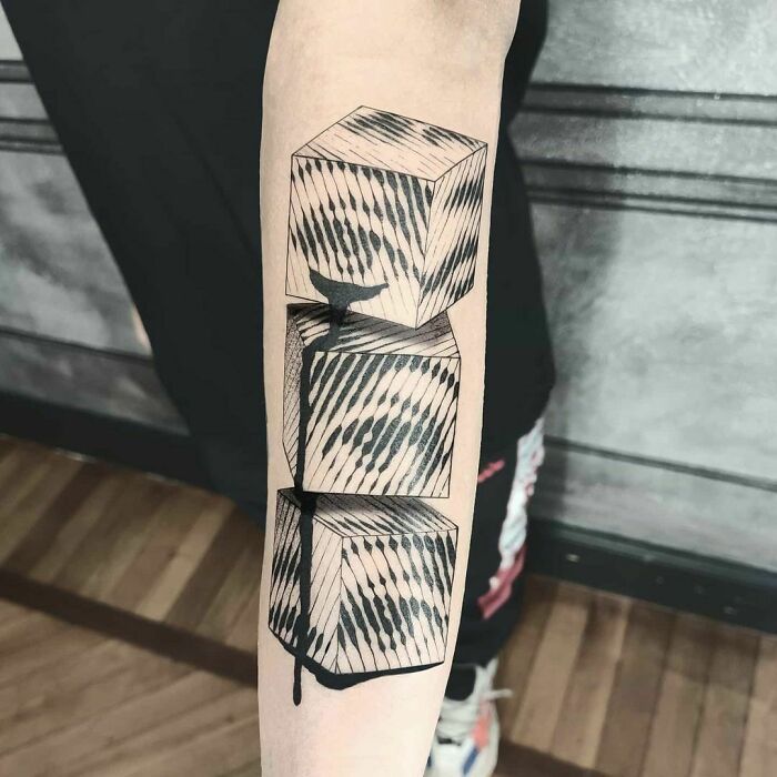 Optical illusion tattoo design of three stacked cubes with striped patterns on a forearm.