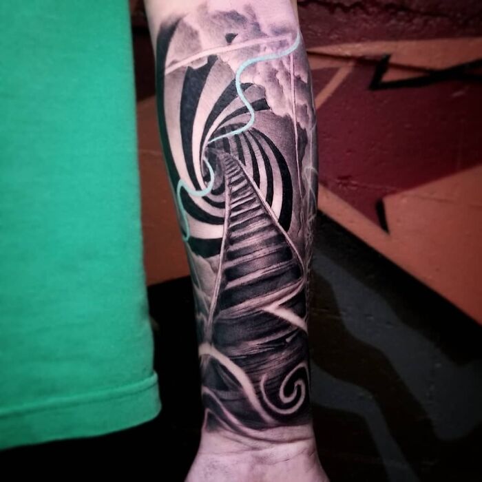 Arm with an optical illusion tattoo featuring a swirling staircase, showcasing intricate black and white patterns.