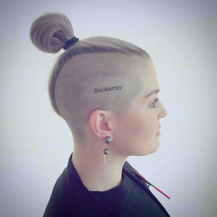 Star with a side-shaved head tattoo reading "Solidarity," styled with an updo and earrings.