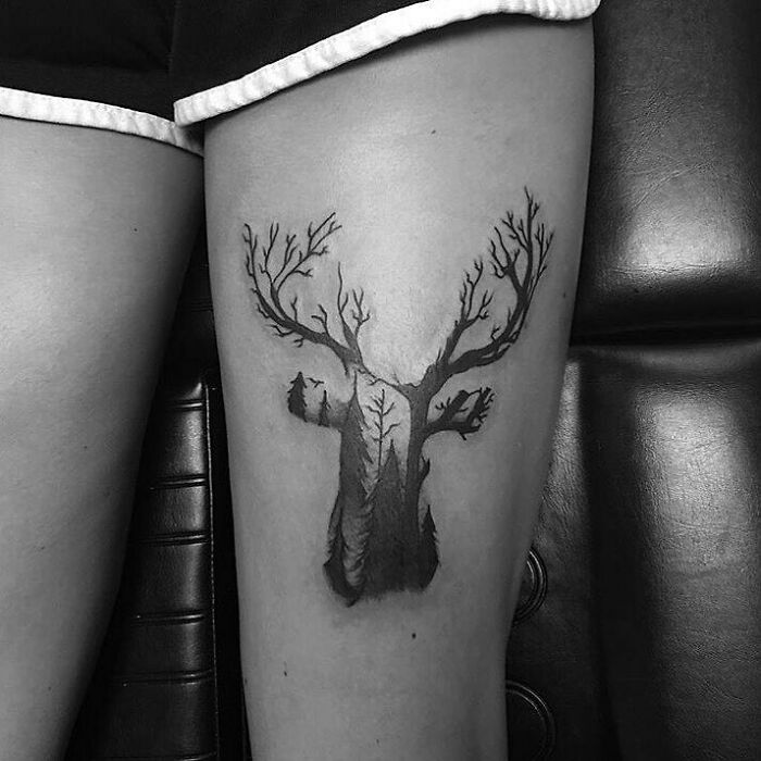 Optical illusion tattoo on thigh, depicting a deer with tree branches as antlers in a mind-bending design.