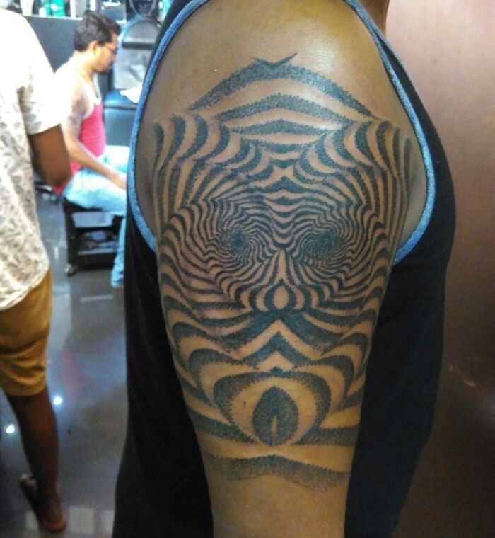Optical illusion tattoo on upper arm with intricate, mind-bending design creating an eye-like effect.