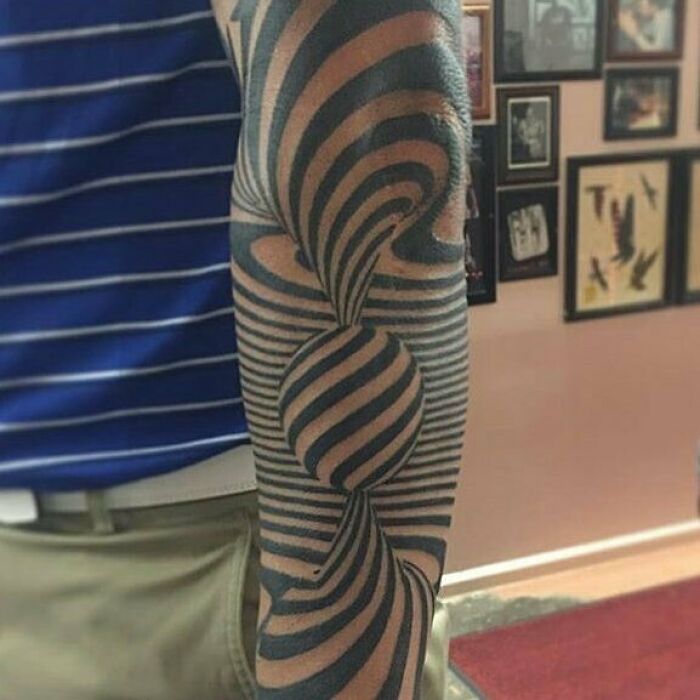 Optical illusion tattoo with stripes creating a 3D effect on a person's arm.