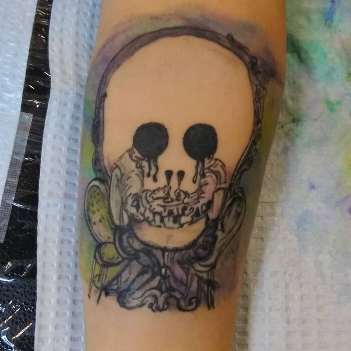 Optical illusion tattoo of a distorted skull design on a person's arm.