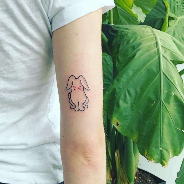 Celebrity tattoo of a minimalist bunny design on a Sophie Turner's arm with a large green leaf in the background.