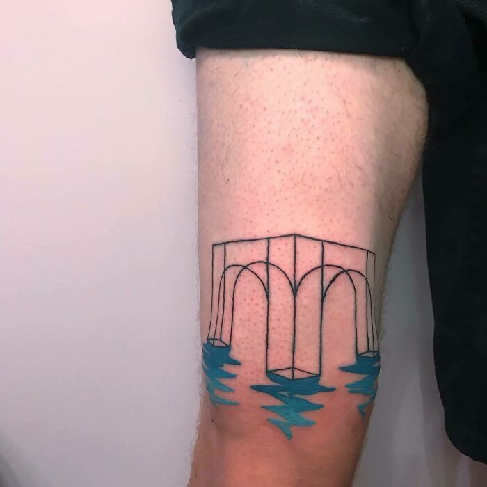 Optical illusion tattoo of an impossible bridge on an arm, with water-like blue elements, creating a mind-bending effect.