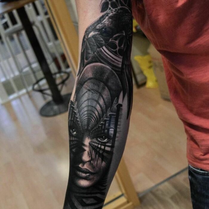 Arm with an intricate optical illusion tattoo design featuring a surreal face and abstract patterns.