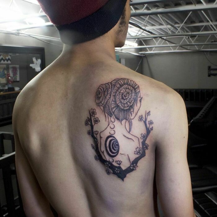 Optical illusion tattoo featuring a spiral design on the back of a person in a studio setting.