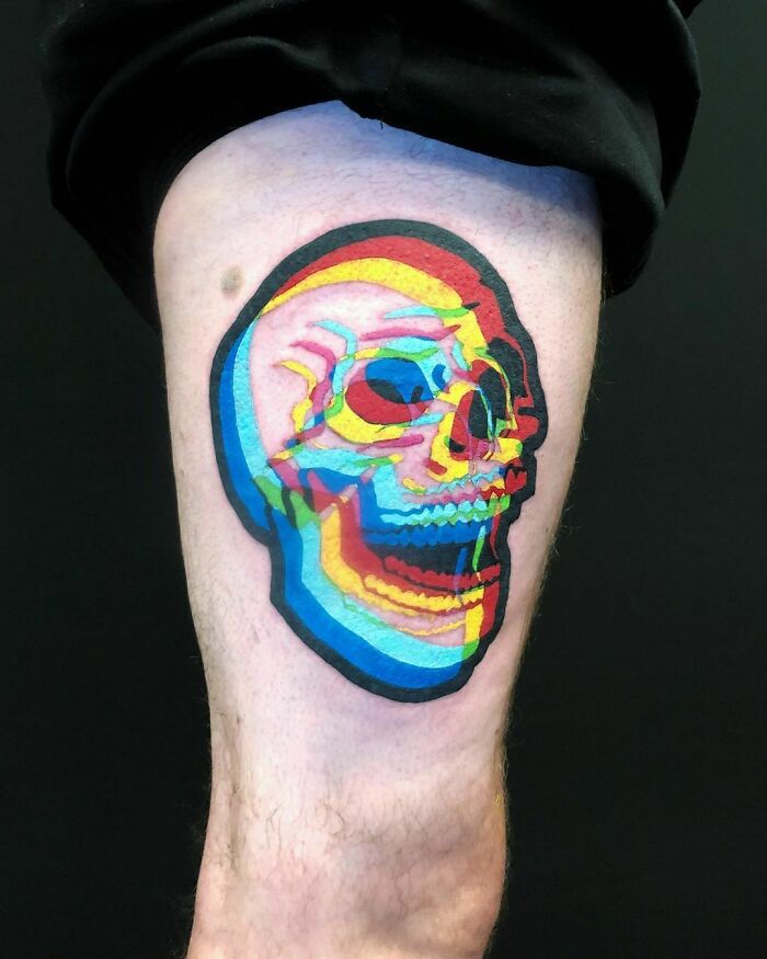 Optical illusion tattoo of a colorful skull on a person's leg, showcasing vibrant overlapping colors.