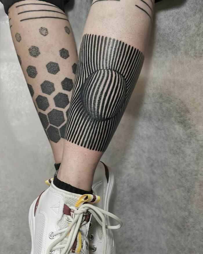 Arm with optical illusion tattoos featuring hexagons and vertical lines, creating a 3D effect, showcased on a leg.