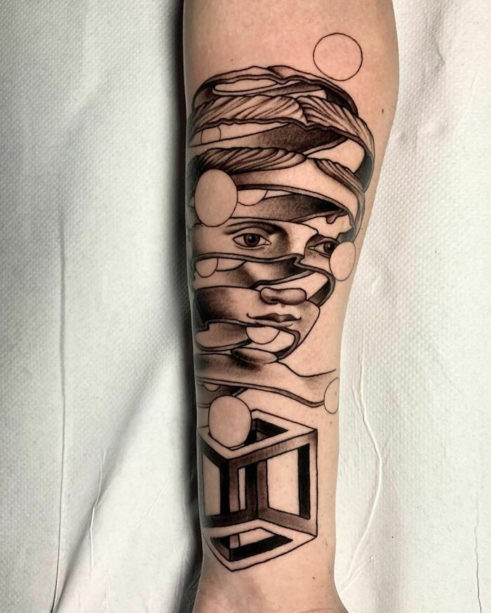 Optical illusion tattoo design of a fragmented face and geometric shapes on an arm.