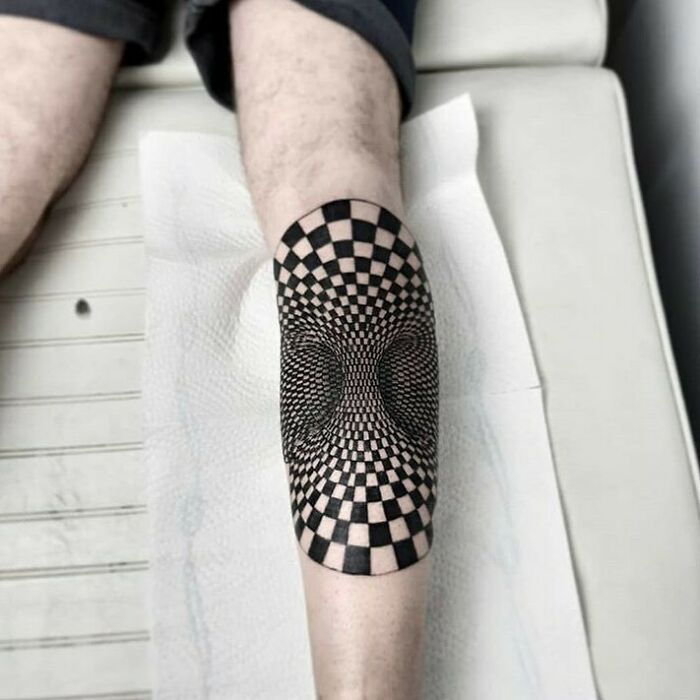 Optical illusion tattoo with a 3D checkered design on a leg.