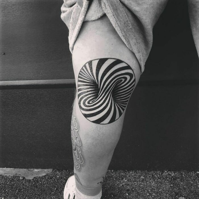 Optical illusion tattoo on leg with swirling black and white pattern.