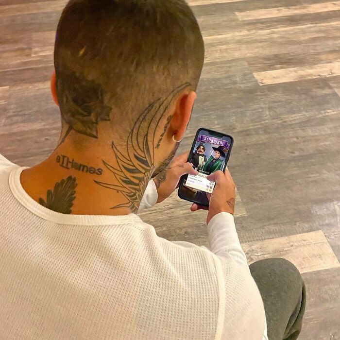Man with intricate neck tattoos, including a star design, looking at a smartphone.