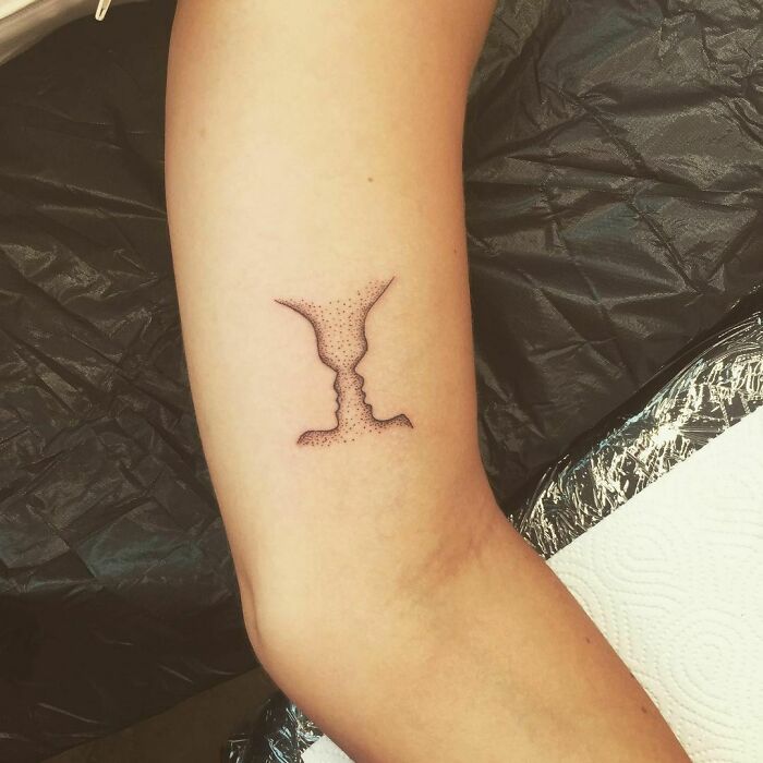 Optical illusion tattoo of a vase and two faces on an arm, highlighting mind-bending design elements.