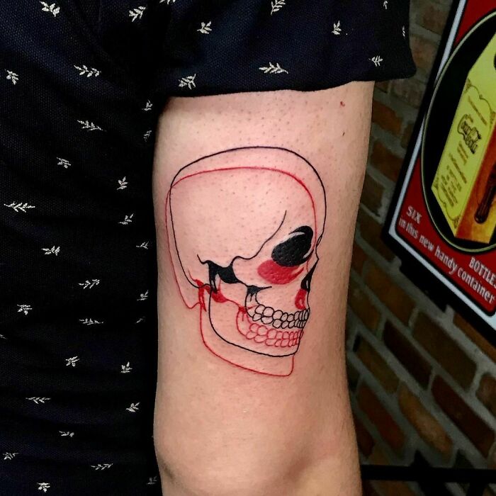 Optical illusion tattoo of a skull in red and black ink on an upper arm, showing eye and mind-bending design.