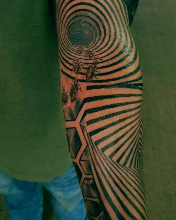 Optical illusion tattoo on an arm, featuring spirals and ants, creating a mesmerizing visual effect.