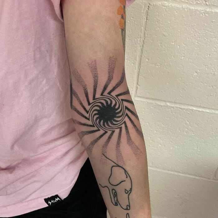Arm with an optical illusion tattoo design, featuring swirling patterns creating a mesmerizing visual effect.