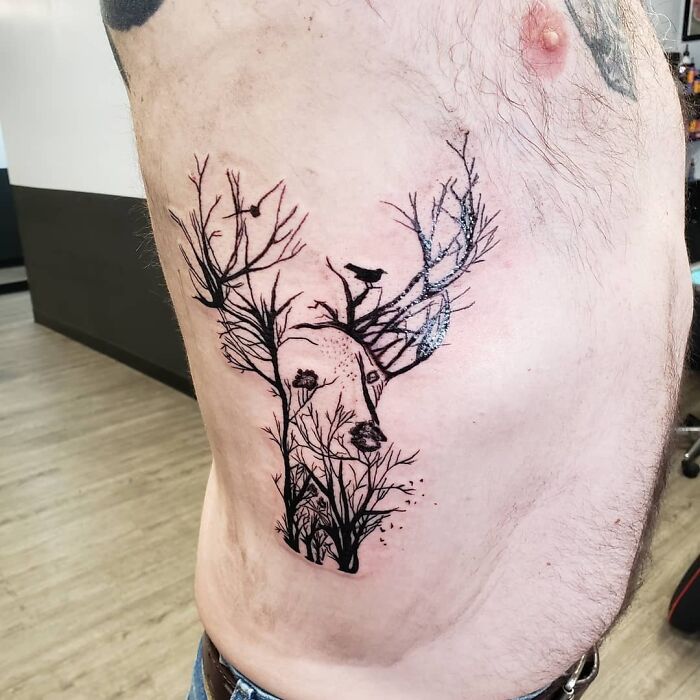 A deer-shaped optical illusion tattoo with branches and birds on a person's side.