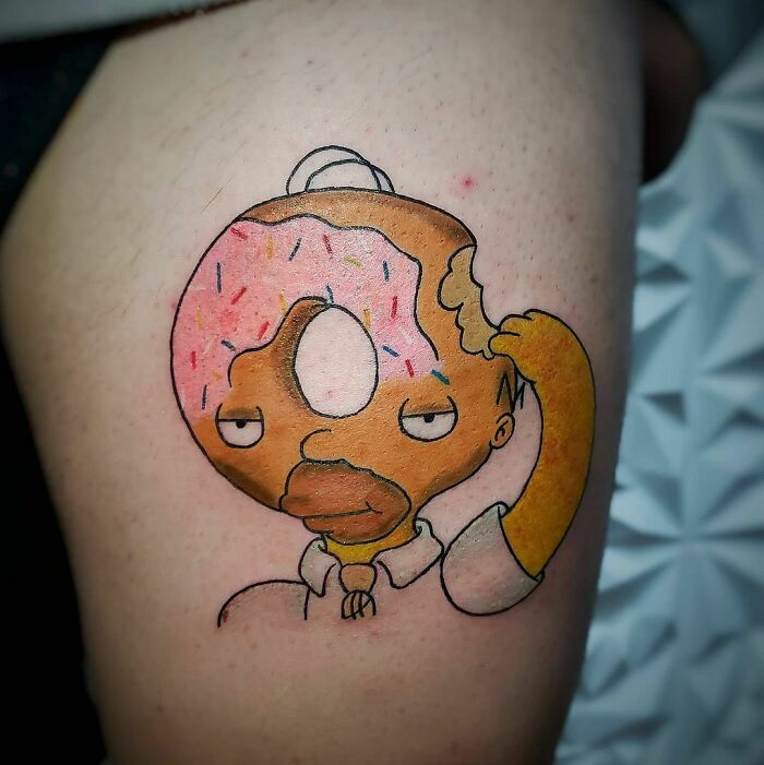 Funny tattoo of a cartoon character's head as a donut with sprinkles and a bite taken out.