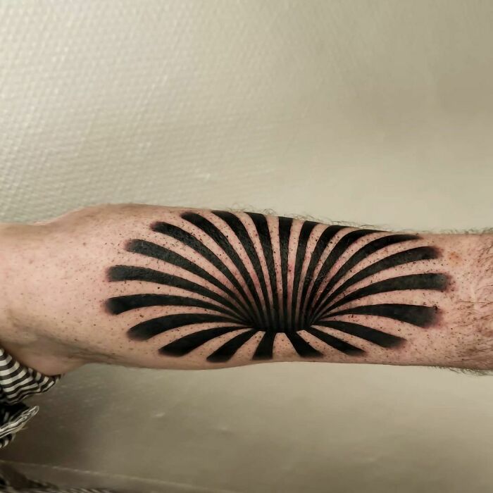 Optical illusion tattoo on an arm with black geometric design creating a 3D effect.