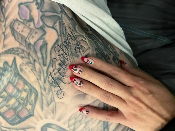 Close-up of detailed celebrity tattoos with a hand showcasing red and white patterned nails.