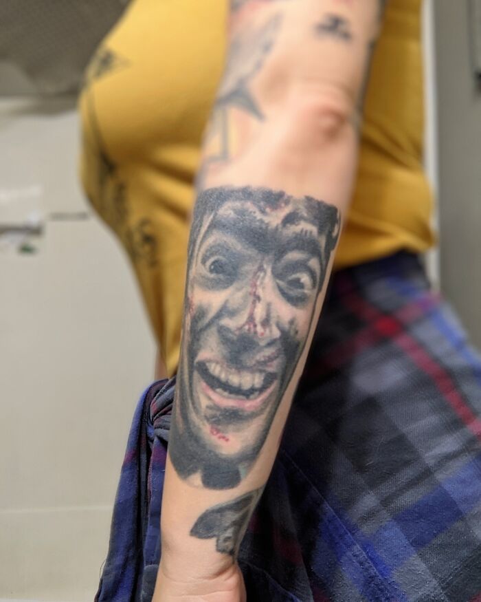 Aged tattoo on a forearm showing how tattoos change over time, featuring a detailed face design.