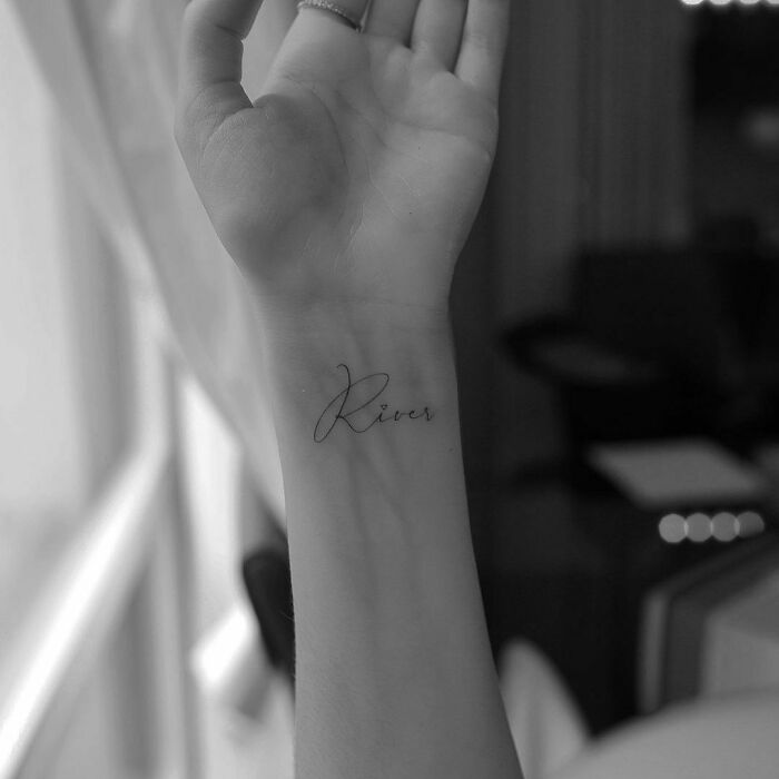 Celebrity tattoo "River" inked on a wrist in elegant script.
