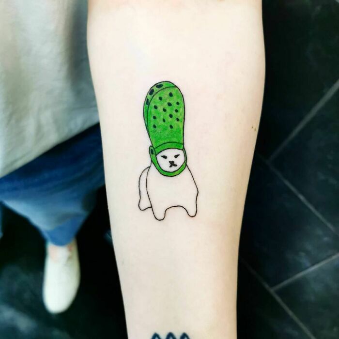 Funny tattoo of a cat with a green Croc on its head on an arm.