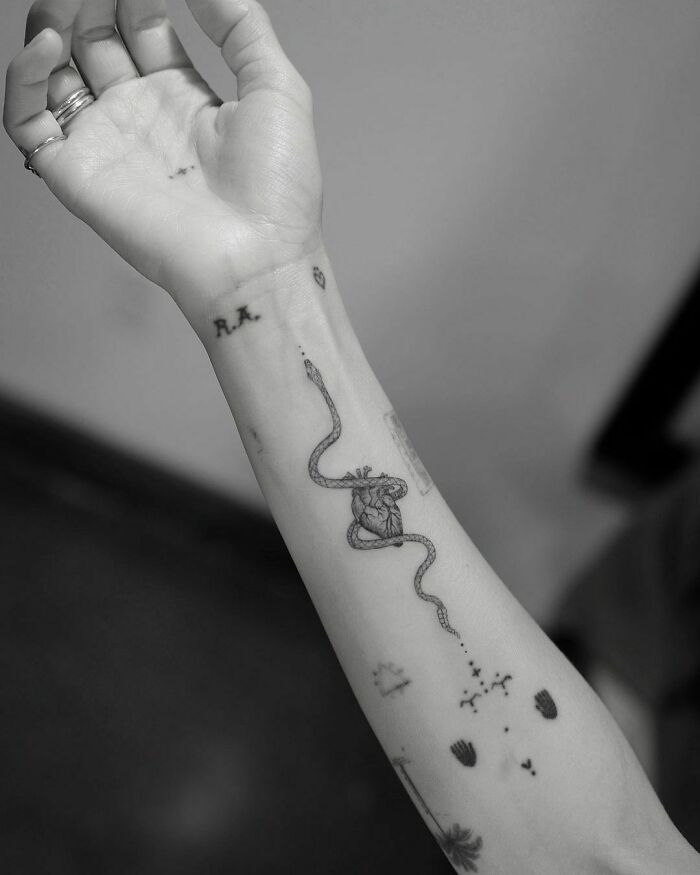 Celebrity tattoo of a snake entwined with a heart on an arm, featuring multiple smaller tattoos around it.