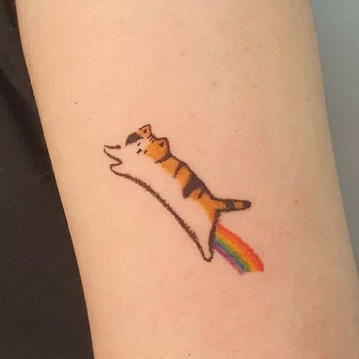 Rainbow cat funny tattoo featuring a leaping cat with a rainbow trail on skin.