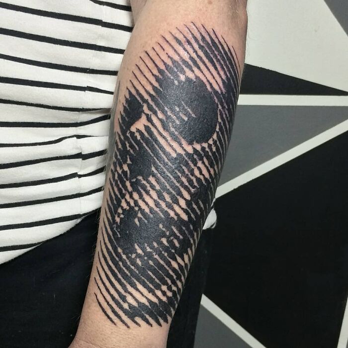 Optical illusion tattoo design of a skull on a forearm, featuring striped patterns and a geometric background.