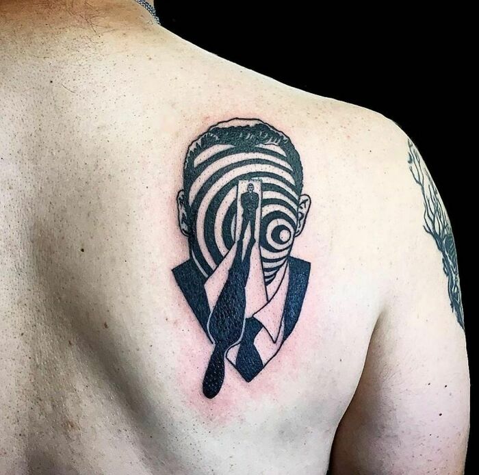Optical illusion tattoo design of a suited figure with a spiral pattern on their head.