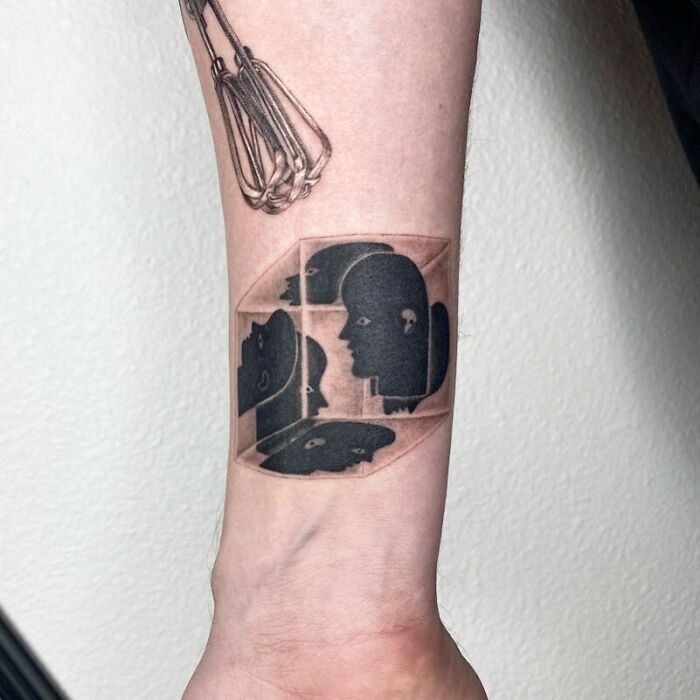 Optical illusion tattoo featuring faces in a 3D cube design on a forearm.