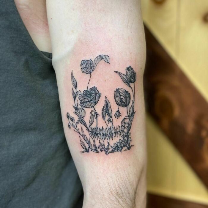 Skull-shaped floral tattoo, featuring optical illusion designs on the inner arm.