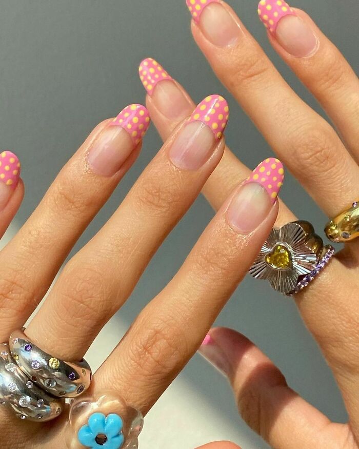 Close-up of hands with pink and yellow polka dot nail art design, showcasing creative nail art ideas and colorful jewelry.