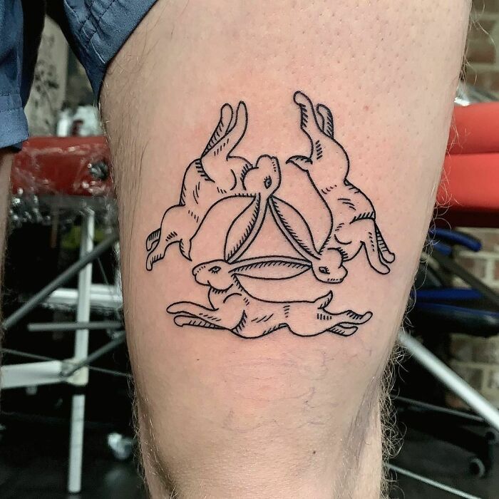 Optical illusion tattoo of three rabbits with shared ears on a person's thigh.