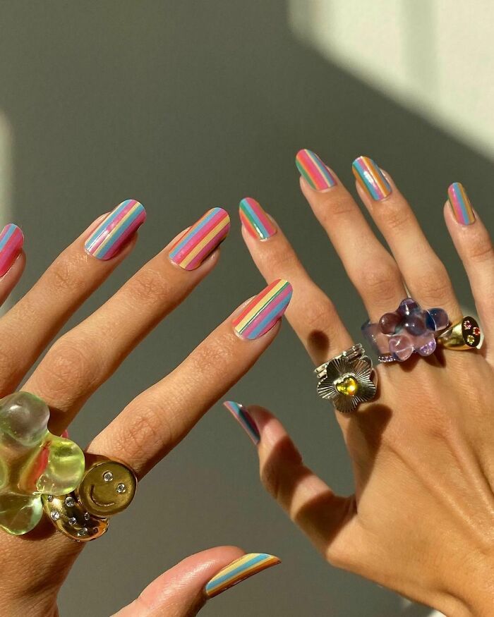 Colorful striped nail art on hands with playful rings under sunlight.