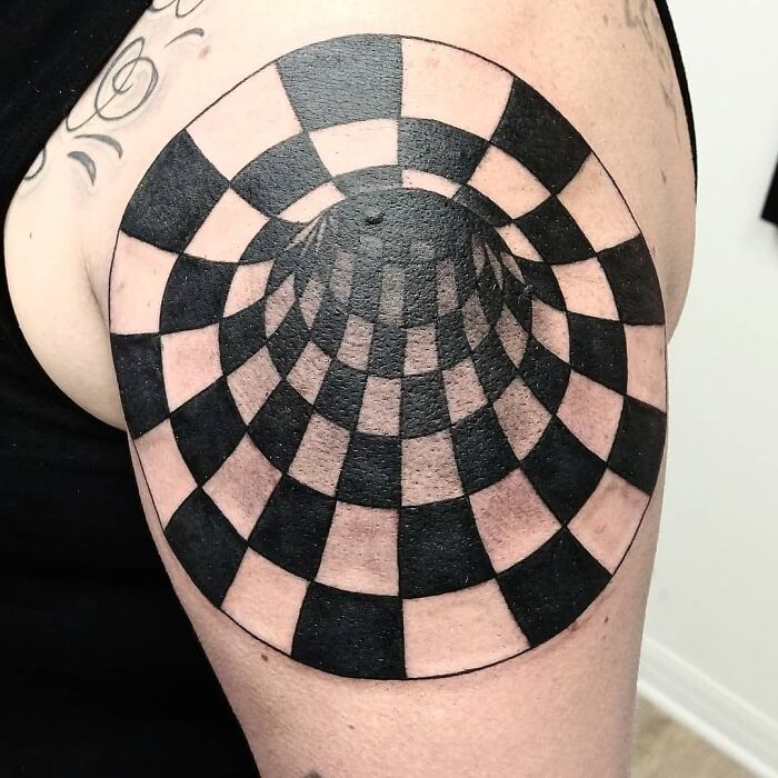 Optical illusion tattoo of a 3D checkered pattern on a person's arm.