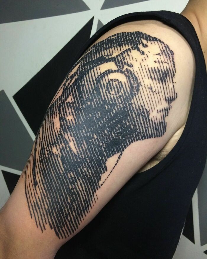 Optical illusion tattoo of a face on an arm with mind-bending design lines.