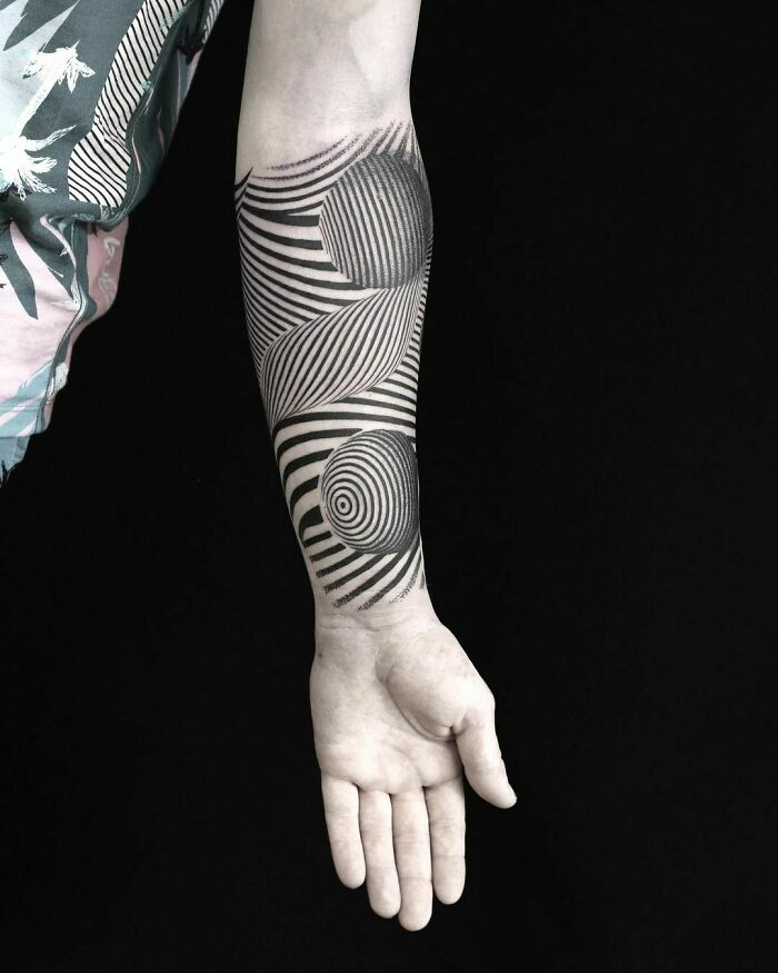 Arm with optical illusion tattoo featuring swirling black and white patterns.