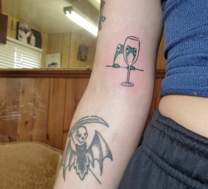 Optical illusion tattoo of creatures peeking through a wine glass on arm.