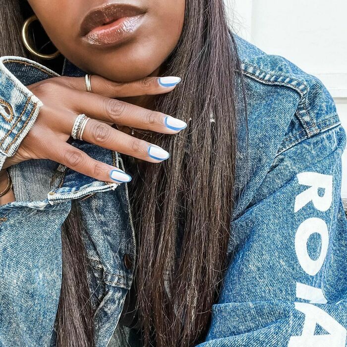 Close-up of nails with minimalist blue and white nail art showcasing creative nail art ideas on a hand wearing rings and denim jacket.