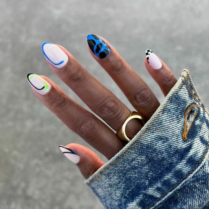 Hand with multi-colored abstract nail art designs featuring blue, black, and neon accents, highlighting creative nail art ideas.