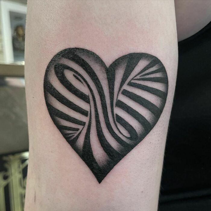 Heart-shaped optical illusion tattoo with black stripes on skin.