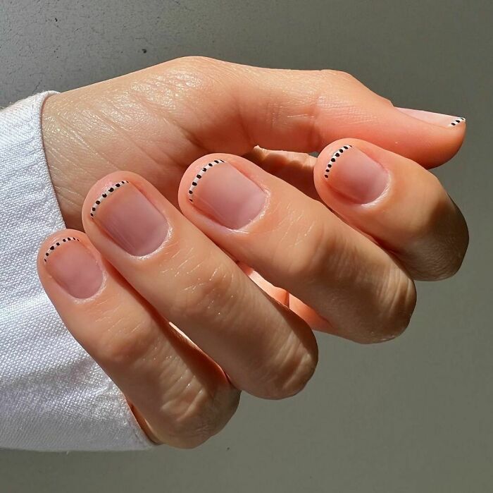 Hand with minimalist nail art ideas featuring tiny black dots along the nail tips for stylish nail designs.